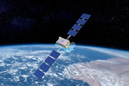 A satellite with blue solar panels orbits Earth, with the planet's surface and atmosphere visible in the background against a backdrop of stars in space, highlighting innovations showcased at the Small Satellite Conference 2023.