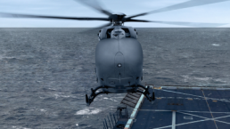 A helicopter hovers over the edge of an aircraft carrier at sea. The gray helicopter, possibly part of a USMC Aerial Logistics Connector contract, has its rotors in motion, while the vast ocean extends to the horizon under a cloudy sky. The aircraft carrier's deck is partially visible with markings and a safety net.